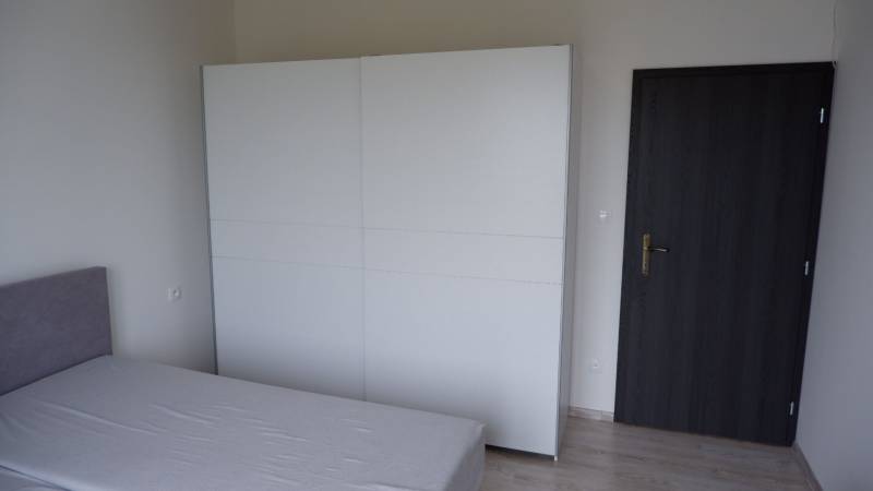 Egy családi ház szobája ággyal, fehér szekrénnyel és sötét ajtókkal.