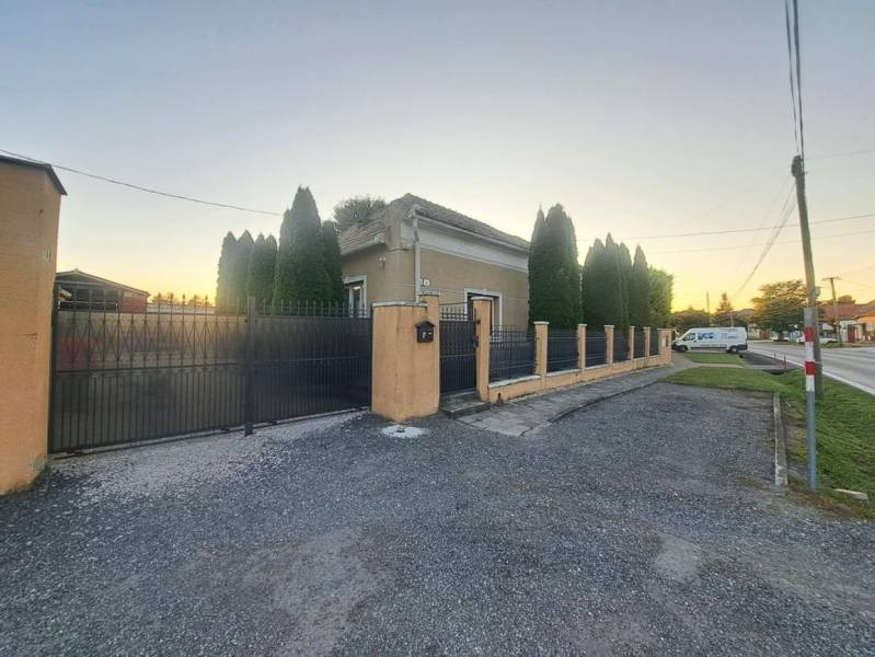 Családi ház Gútán magas tujafákkal és fém kerítéssel az út mellett.