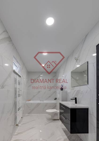 Fürdőszoba egy családi házban kerámia falakkal és káddal, fekete mosdóval és tükörrel.