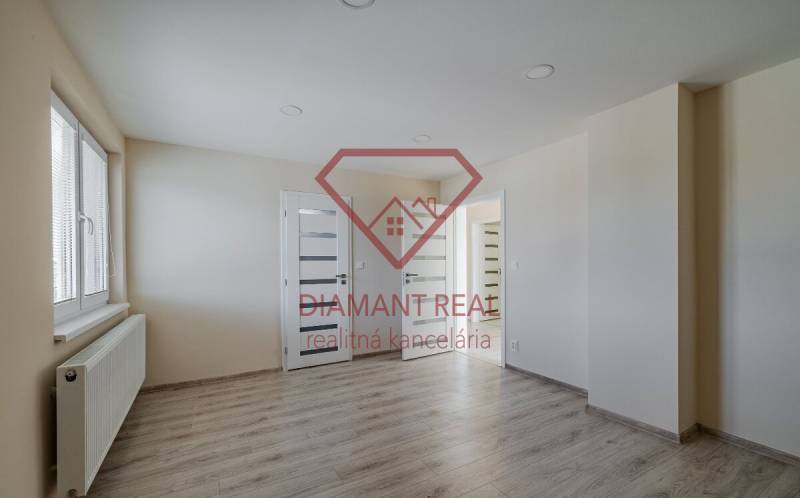 Szoba egy családi házban fa dekorációjú padlóval, világos falakkal és ablakkal.