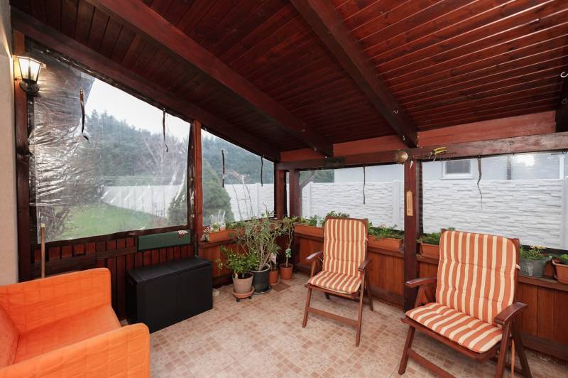 Családi ház télikertje székekkel és növényekkel, csempézett padlóval.