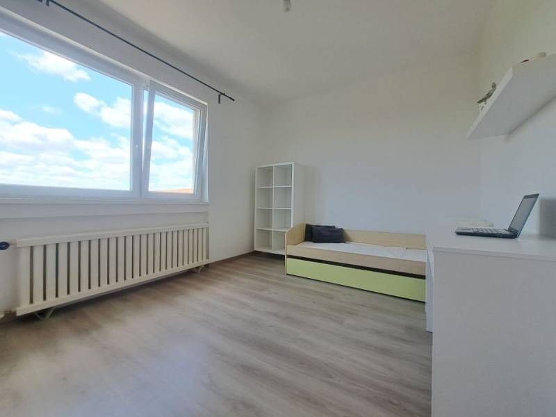 Világos szoba polcokkal, kinyitható ággyal és ablakkal egy családi házban, fa dekoros padlóval.