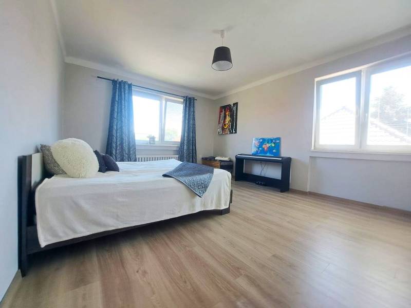 Szoba ággyal, két ablakkal, zongorával és fa dekorációjú padlóval egy családi házban.