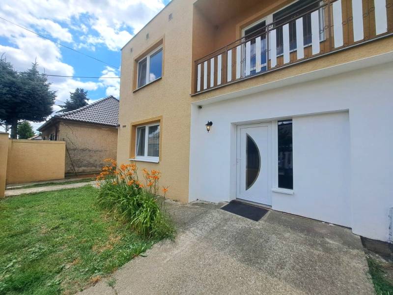 Családi ház Nagymácsédon narancssárga virágokkal, zöld gyepével és bejárati ajtóval.