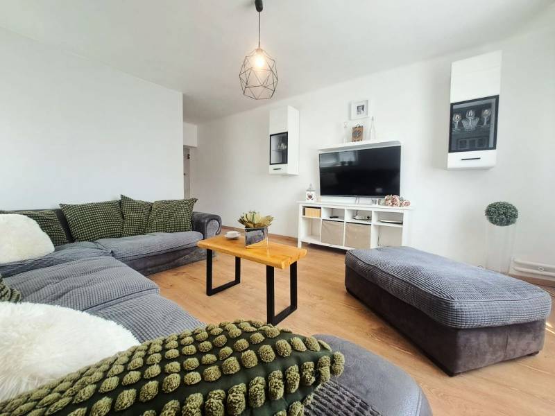 Nappali egy családi házban, fa mintázatú padlóval és kényelmes ülőgarnitúrával.