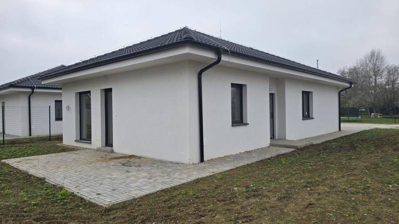 Családi ház Cíferen ferde tetővel és burkolt terasszal a kertben.