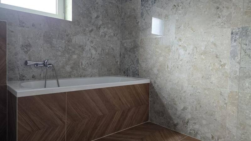 Fürdőszoba családi házban káddal, kőmintás csempékkel, fa dekoros padlóval.