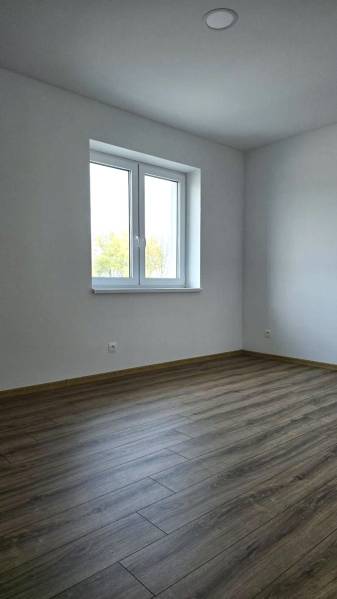 Szoba egy családi házban, fa mintázatú padlóval és fehér falakkal.