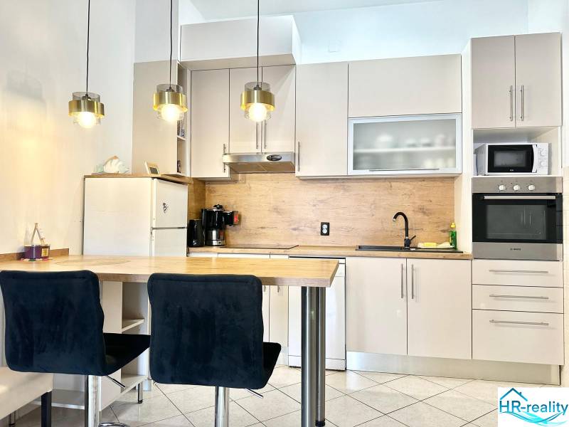 Konyha üdülő apartmanban bárpulttal, függő lámpákkal és fehér szekrénnyel.