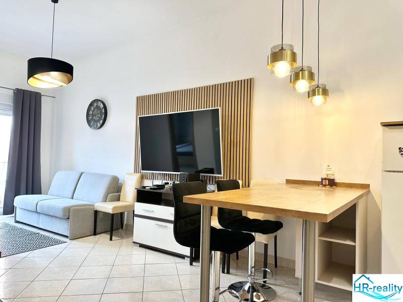 Nappali rekreációs apartman televízióval, kanapéval és bárszékekkel.