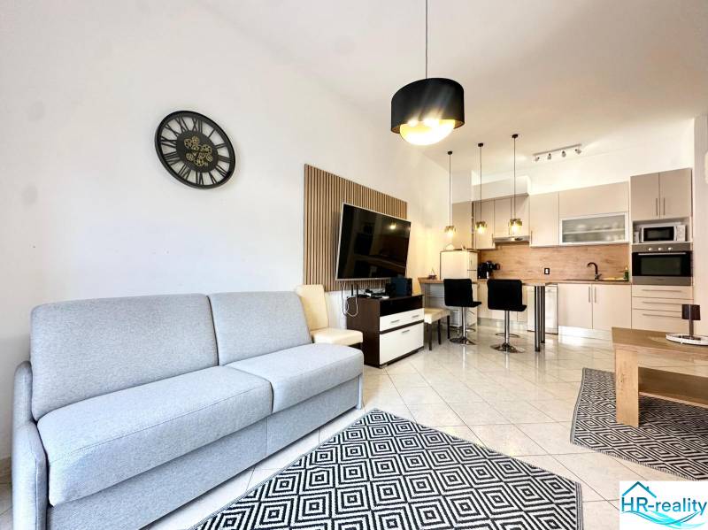 Világos nappali konyhával, kanapéval, televízióval és étkező sarokkal az üdülő apartmanban.