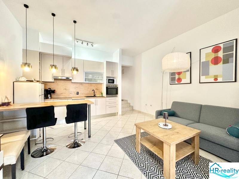 Nyaraló apartman konyhasarokkal, étkezőasztallal, kanapéval és művészeti képekkel a falon.