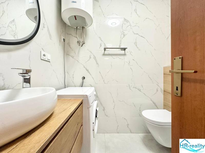 Fürdőszoba egy üdülő apartmanban WC-vel, mosógéppel és mosdókagylóval fa dekorációval.