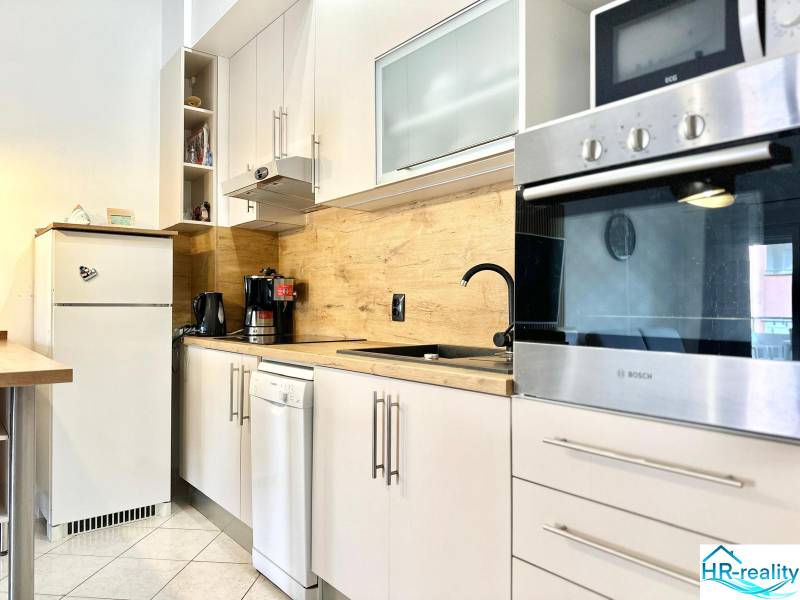 Konyha a nyaraló apartmanban fehér bútorokkal és fa dekorációval a falon.