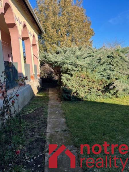 Családi ház Tomášovcén előkerttel és nagy fával a járda mellett.