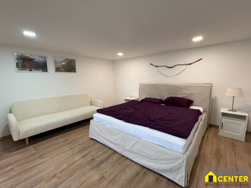 Hálószoba egy egyszobás lakásban kanapéval, ággyal és fa dekorációjú padlóval.