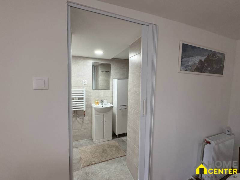 Fürdőszoba egy egyszobás lakásban mosdóval, tükörrel és radiátorral a falon.