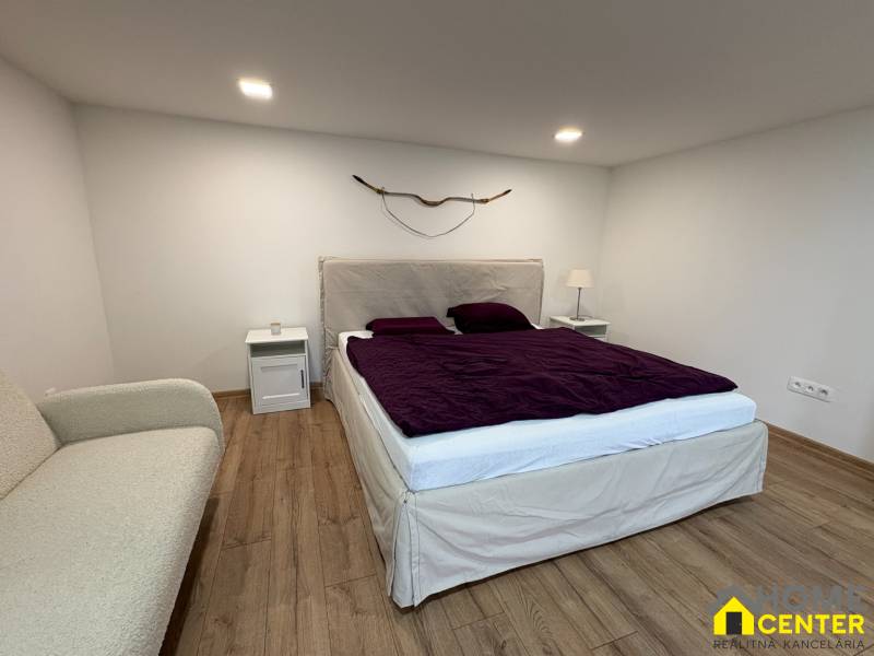 Hálószoba egy egyszobás lakásban fa dekor padlóval, ággyal és dekoratív elemmel a falon.