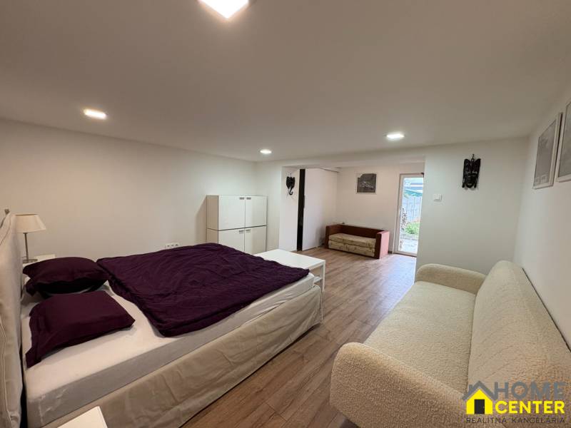 Hálószoba egy egyszobás lakásban fa dekor padlóval, egyszerű bútorokkal és dekorációkkal.