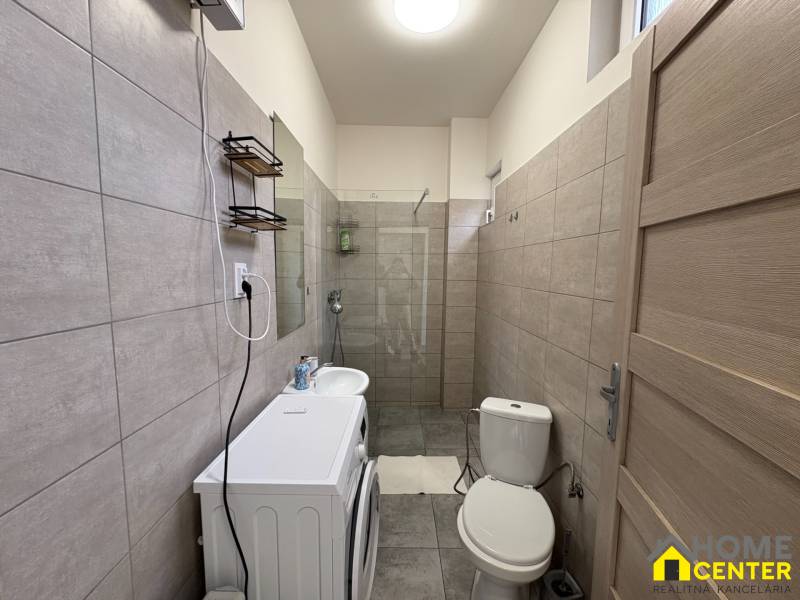 Fürdőszoba egy egyszobás lakásban mosógéppel, mosdóval és zuhanyzóval semleges árnyalatokban.