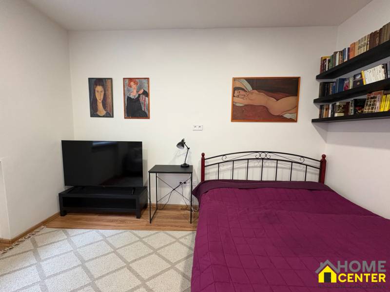 Hálószoba egy egyszobás lakásban, tévével és képekkel a rideg falakon.