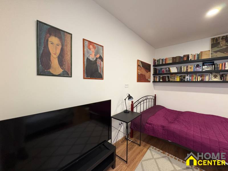 Egyszobás lakás ággyal, könyvespolcokkal és televízióval, fa dekorációjú padlóval.