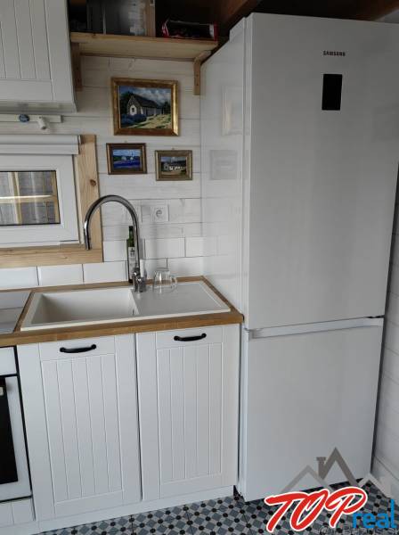 Konyha családi házban fehér konyhabútorral, hűtőszekrénnyel és művészi képekkel a falon.