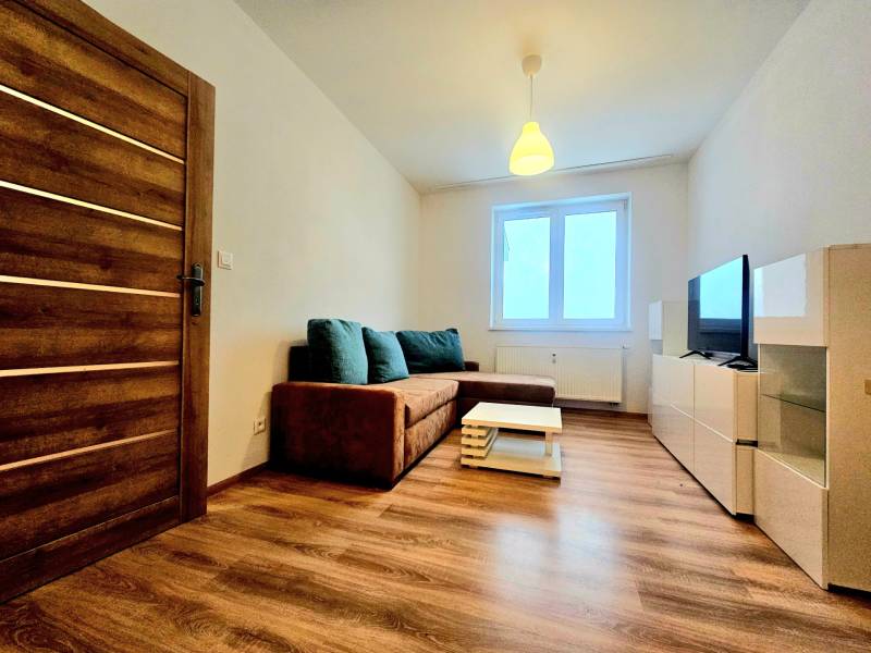 Nappali egy kétszobás lakásban kanapéval és fa mintázatú padlóval.