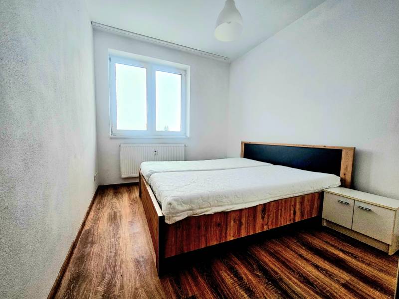 Hálószoba egy kétszobás lakásban fa dekor padlóval, ággyal és ablakkal.