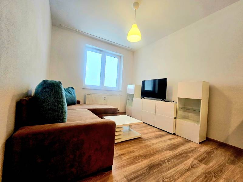 Nappali egy kétszobás lakásban kanapéval, televízióval és fa dekorációjú padlóval.