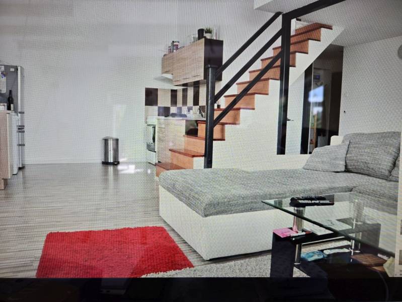 Nappali konyhasarokkal, lépcsővel, kanapéval, üvegasztallal és fa dekorú padlóval.