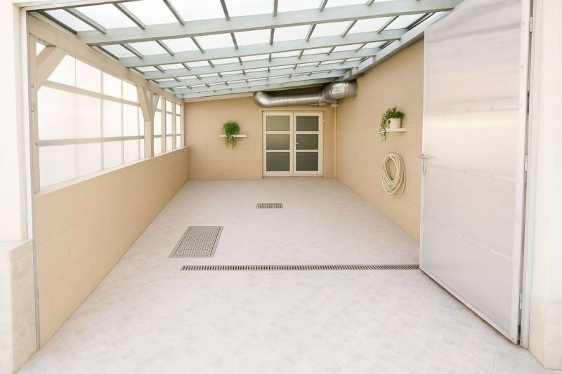 Fedett terasz növényekkel, ajtókkal és csatornával az épületben.