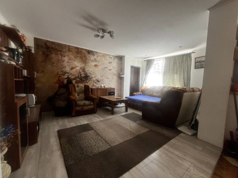 Nappali egy családi házban kanapéval, fotelekkel és falfestménnyel az ülőgarnitúra mögött.