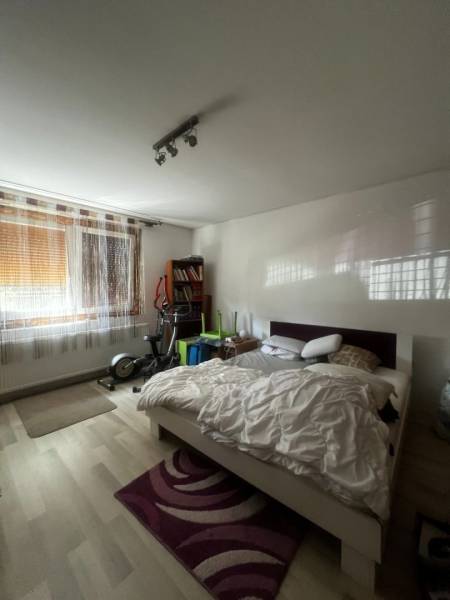 Hálószoba ággyal, edzőgépekkel, könyvespolccal és fa dekoros padlóval egy családi házban.