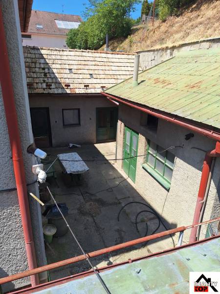 A Tachtoch családi ház udvara látható ajtókkal, asztallal és füves domboldallal.