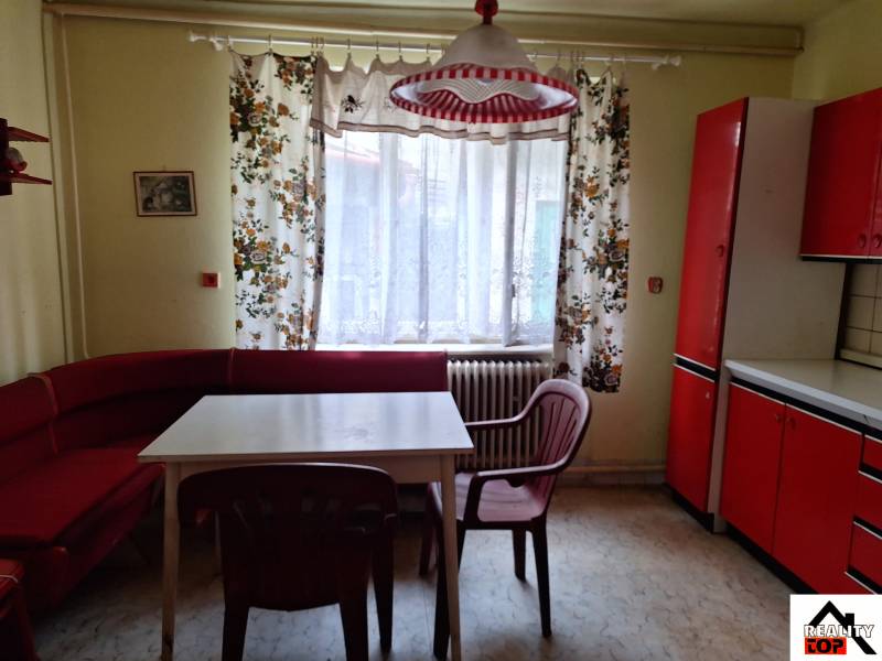 Konyha egy családi házban, piros bútorokkal, színes függönyökkel és műanyag székekkel.