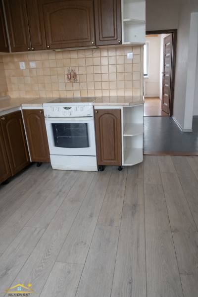 Konyha barna szekrényekkel, fehér tűzhellyel és fa mintázatú padlóval, egy háromszobás lakásban.