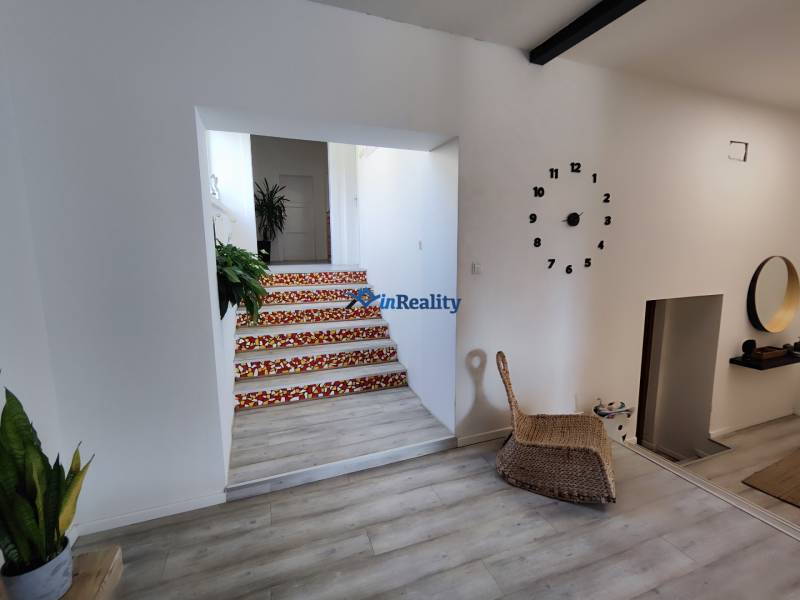 Családi ház belső tere faliórával, fa dekorációjú padlóval és színes mintájú lépcsőkkel.