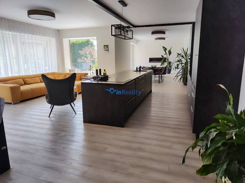 Konyha és nappali családi házban szigettel, sárga kanapéval és fa mintás padlóval.