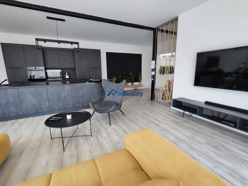 Nappali konyhával egy családi házban, fa dekoros padlóval és sárga kanapéval.