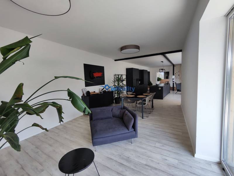 Nappali egy családi házban, fa mintázatú padlóval, szürke bútorokkal és növénnyel.