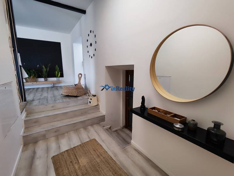 Családi ház belső tere fa dekorációjú padlóval, kerek tükörrel és szobanövényekkel.