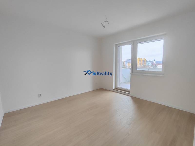 Üres szoba egy kétszobás lakásban, fa mintázatú padlóval és erkélyajtóval.