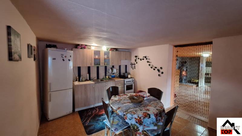 Családi ház konyhája étkezőasztallal, konyhapulttal és hűtőszekrénnyel.