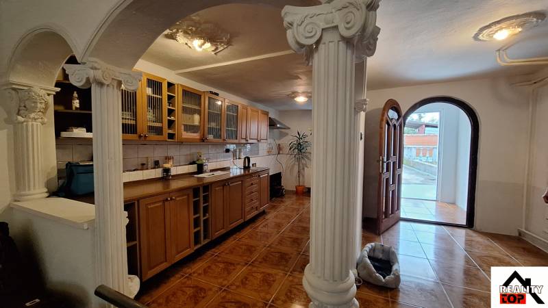 Családi ház belső tere fa konyhabútorral, oszlopokkal és fa dekorációjú padlóval.