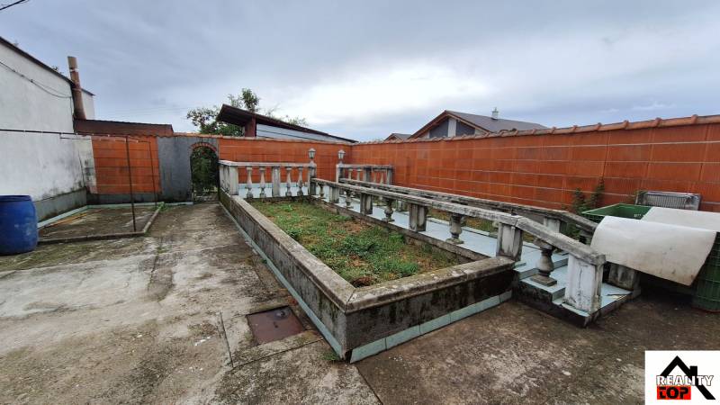 A Zacharovce-i családi ház udvara virágágyással és beton járdával.