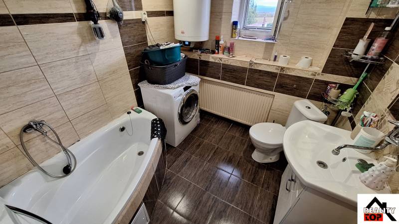 Fürdőszoba családi házban káddal, mosógéppel és dekoratív barna csempékkel.