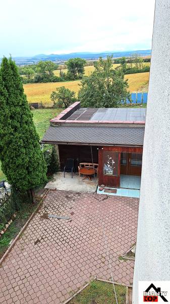 A Zacharovce-i családi ház kertje pavilonnal, fákkal és kilátással a mezőre.