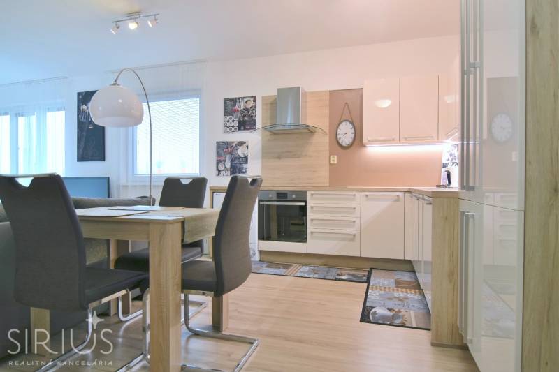 Modern konyha étkezőasztallal, fehér szekrényekkel és fa dekorációjú padlóval egy kétszobás lakásban.