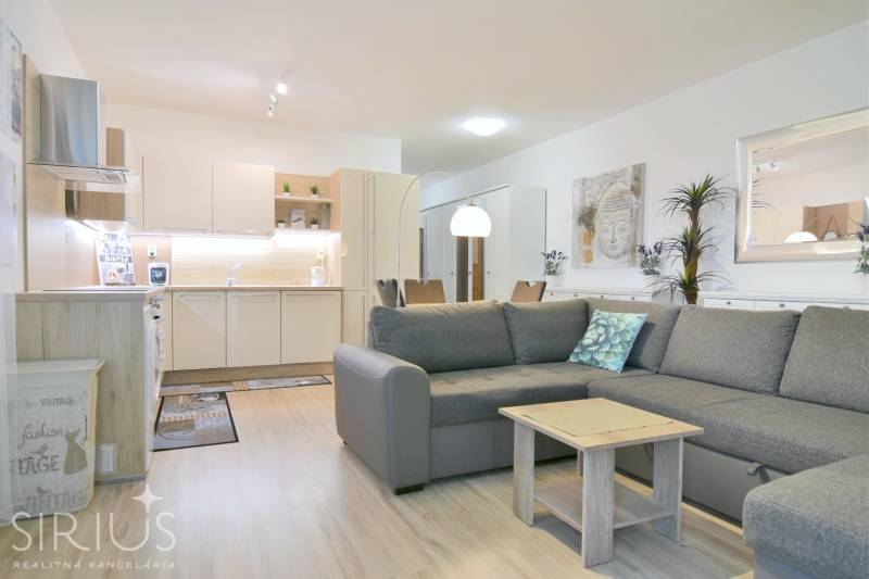 Nappali konyhasarokkal és fa dekorú padlóval egy kétszobás lakásban.